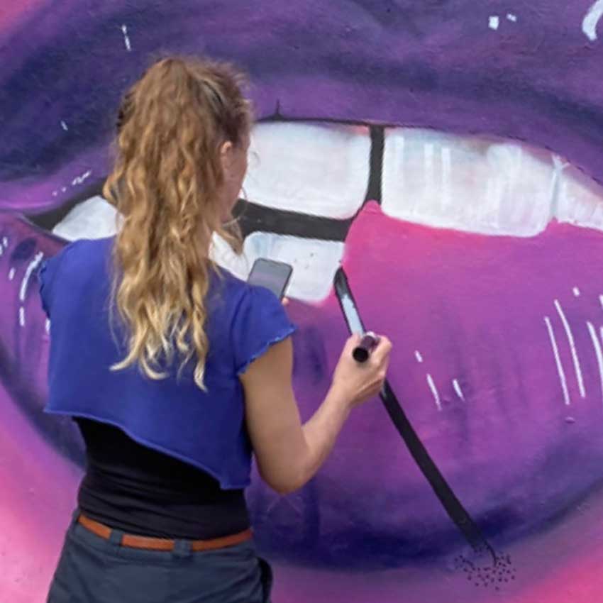 Street artist Amanda Rigby painting a huge purple lip mural in Peterborough